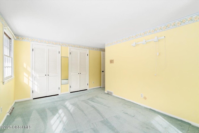 unfurnished bedroom with light colored carpet and multiple closets