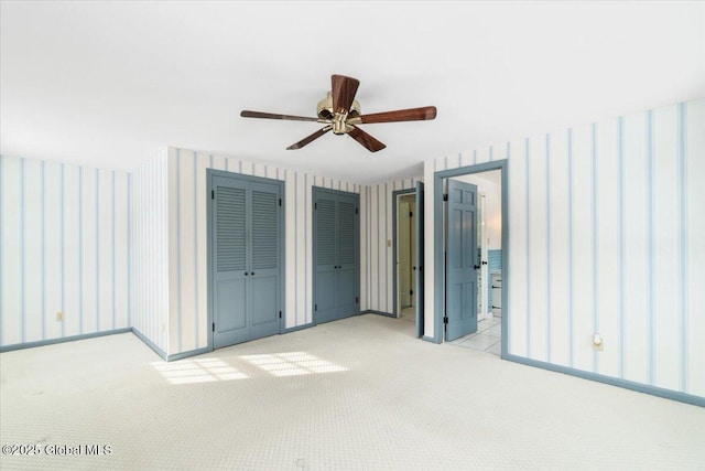 unfurnished bedroom featuring multiple closets, ceiling fan, light colored carpet, and ensuite bath