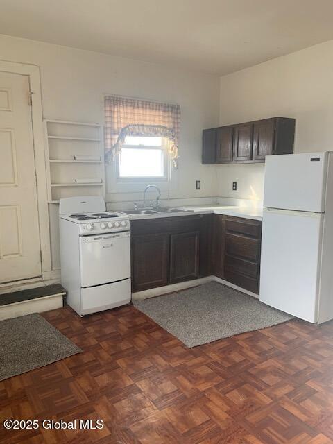 kitchen with dark brown cabinetry, sink, white appliances, and dark parquet flooring