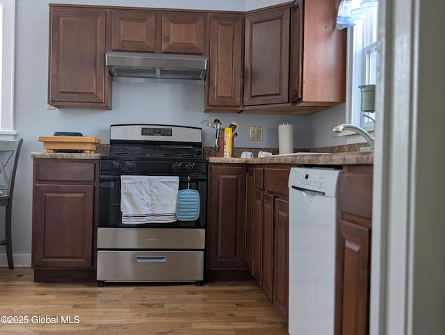 kitchen with under cabinet range hood, dark stone counters, light wood-style floors, dishwasher, and stainless steel range with gas stovetop