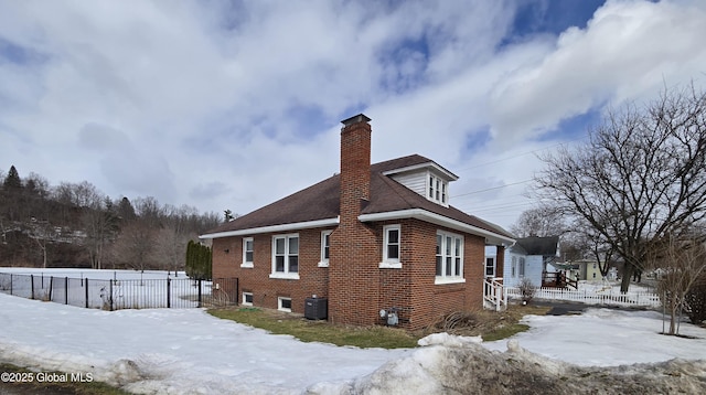 snow covered property featuring central AC unit, a chimney, fence, and brick siding