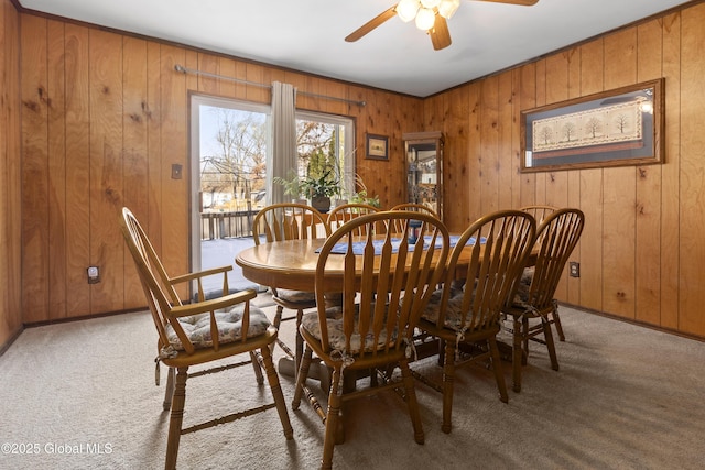 carpeted dining space featuring wooden walls and ceiling fan