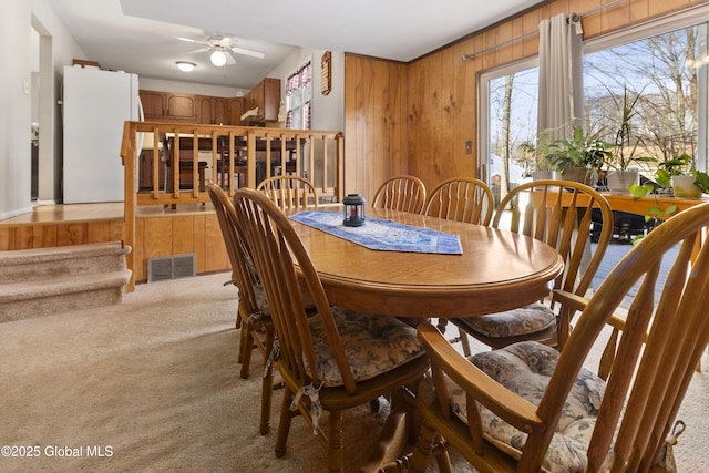 dining area featuring ceiling fan, carpet, and wooden walls