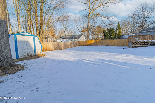 yard layered in snow featuring a deck and a storage unit