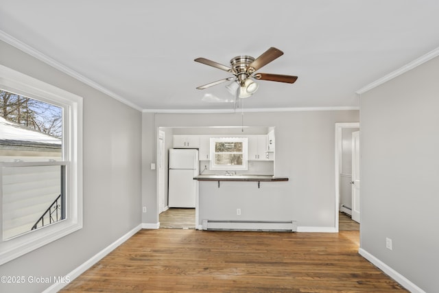 unfurnished living room featuring crown molding, a baseboard heating unit, dark wood-type flooring, and ceiling fan