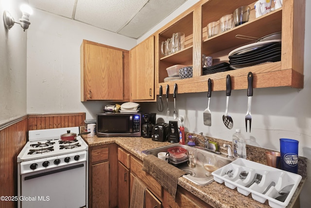 kitchen with a drop ceiling, wooden walls, and white range with gas stovetop