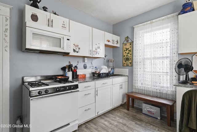 kitchen with sink, white appliances, white cabinetry, hardwood / wood-style floors, and dark stone counters