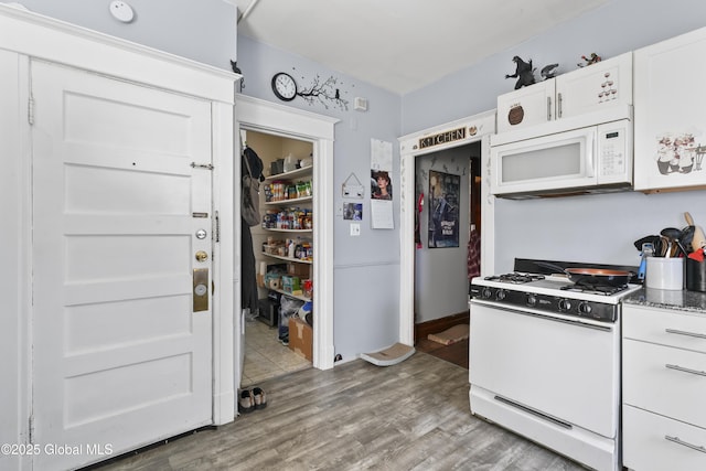 kitchen with white appliances, wood-type flooring, dark stone counters, and white cabinets