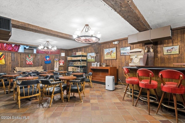 dining space featuring a textured ceiling, wooden walls, beamed ceiling, and indoor bar