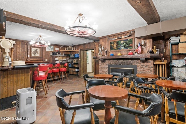 dining space with a textured ceiling, indoor bar, wooden walls, beamed ceiling, and a fireplace