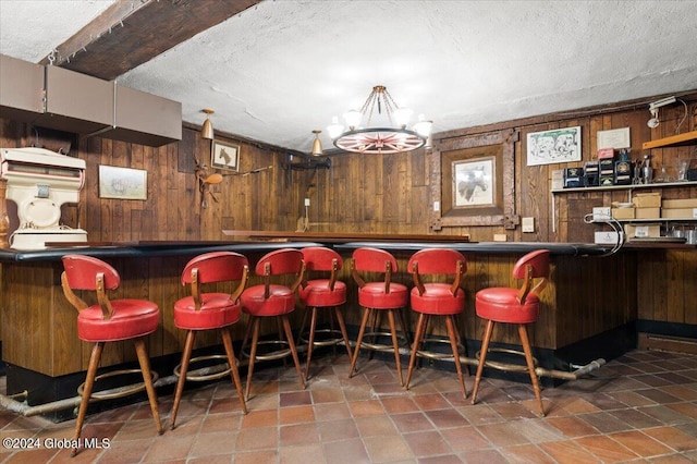 bar with a notable chandelier, a textured ceiling, and wood walls