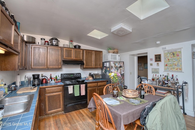 kitchen featuring sink, stainless steel refrigerator, tile counters, black / electric stove, and light wood-type flooring