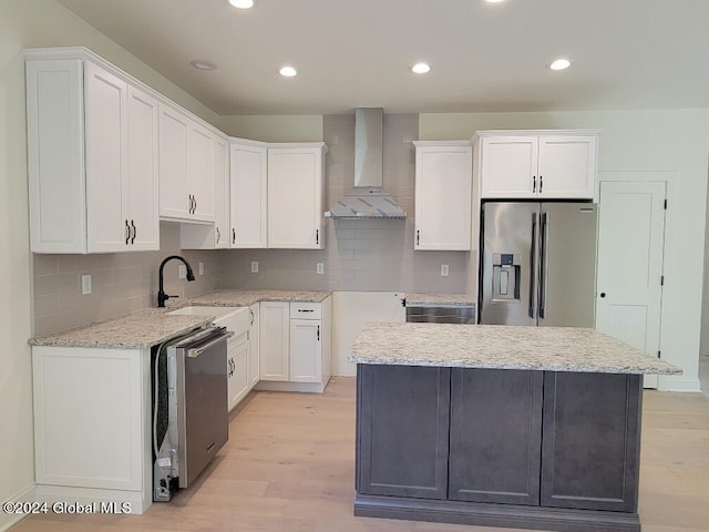 kitchen featuring wall chimney range hood, sink, stainless steel appliances, white cabinets, and light wood-type flooring