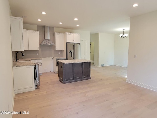 kitchen with a kitchen island, white cabinetry, sink, high end fridge, and wall chimney range hood