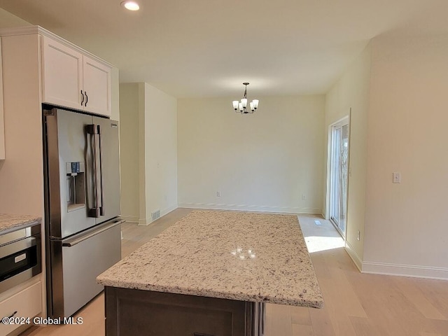 kitchen featuring stainless steel fridge, white cabinetry, hanging light fixtures, a notable chandelier, and light stone countertops