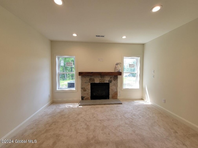 unfurnished living room featuring light carpet, a stone fireplace, and a wealth of natural light