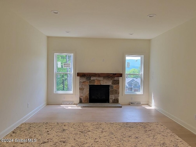 unfurnished living room featuring a stone fireplace and light wood-type flooring