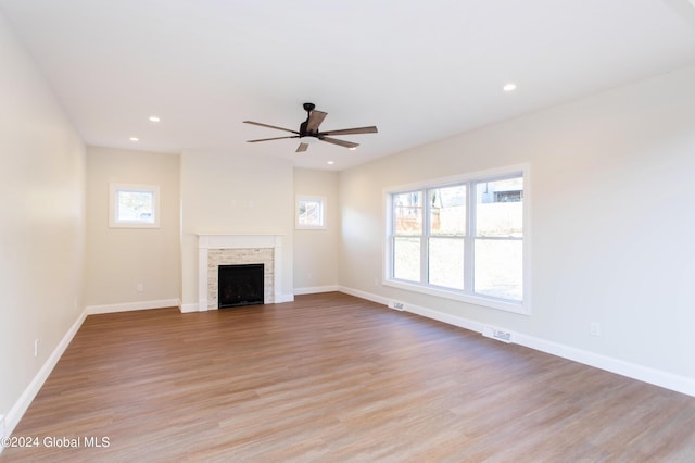 unfurnished living room featuring a stone fireplace, a wealth of natural light, light hardwood / wood-style floors, and ceiling fan