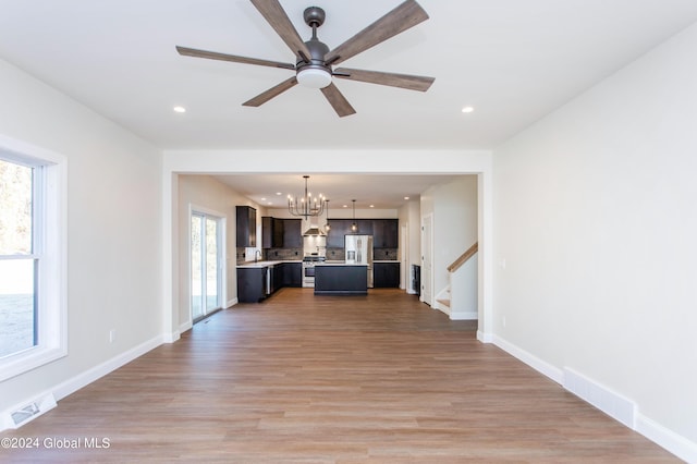 unfurnished living room featuring ceiling fan with notable chandelier and hardwood / wood-style floors