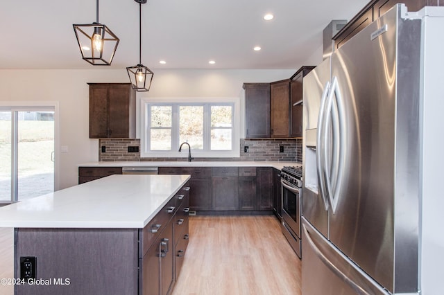 kitchen with a kitchen island, pendant lighting, stainless steel appliances, dark brown cabinets, and light wood-type flooring