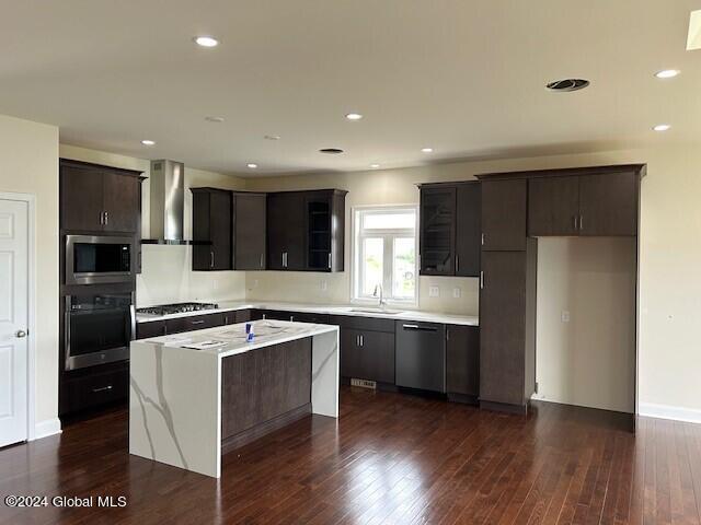 kitchen featuring appliances with stainless steel finishes, sink, a center island, dark brown cabinets, and wall chimney exhaust hood