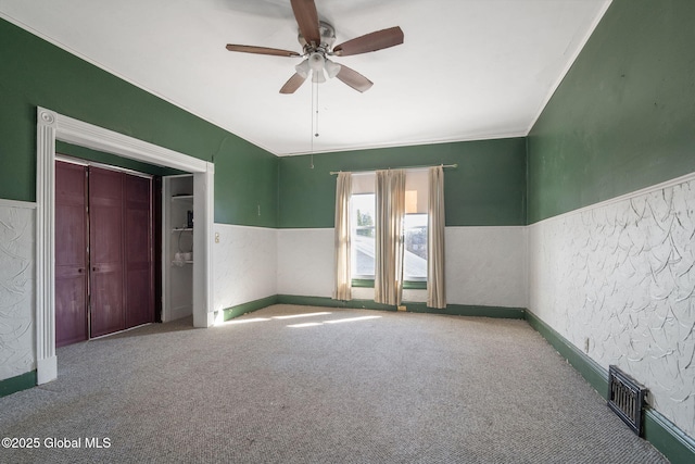carpeted spare room with wainscoting, a ceiling fan, a textured wall, and visible vents