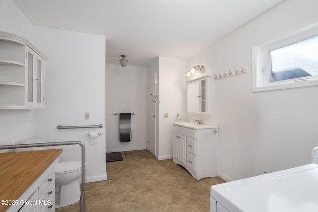 full bath featuring baseboards, toilet, vanity, and washer / clothes dryer
