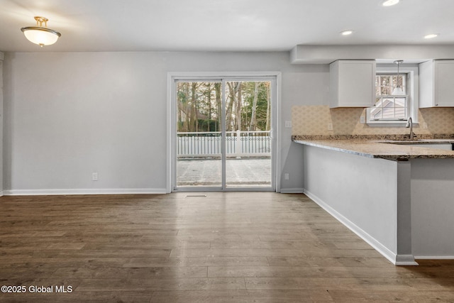 kitchen featuring tasteful backsplash, wood-type flooring, sink, white cabinets, and light stone countertops