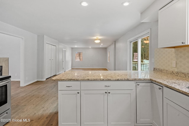 kitchen featuring stainless steel electric range, backsplash, light stone countertops, white cabinets, and kitchen peninsula