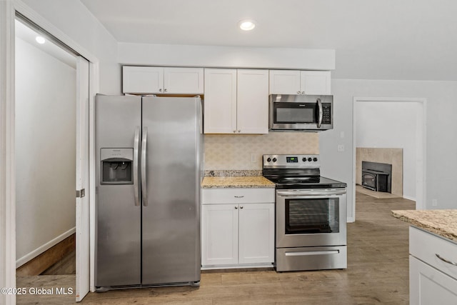 kitchen with appliances with stainless steel finishes, light hardwood / wood-style floors, decorative backsplash, and white cabinets