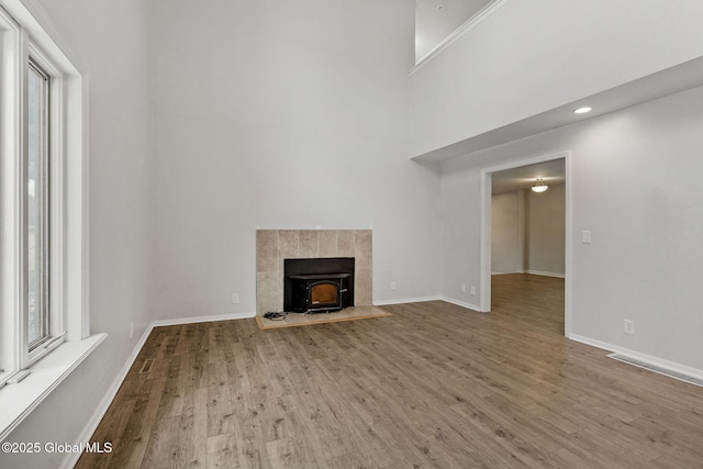 unfurnished living room with wood-type flooring, a wood stove, and a high ceiling