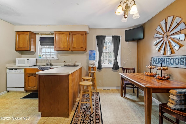 kitchen featuring sink, decorative light fixtures, kitchen peninsula, a notable chandelier, and white appliances