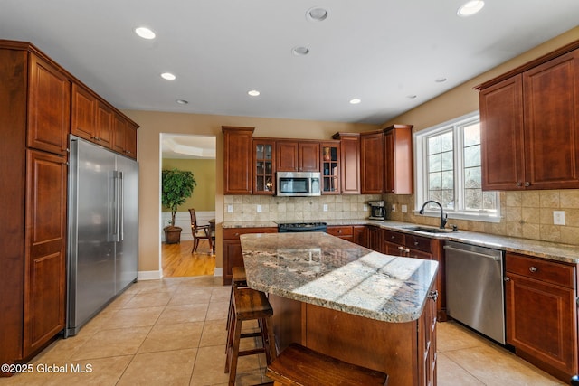 kitchen with a kitchen island, sink, light tile patterned floors, stainless steel appliances, and light stone countertops