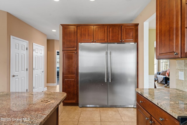 kitchen with light stone counters, backsplash, built in fridge, and light tile patterned floors