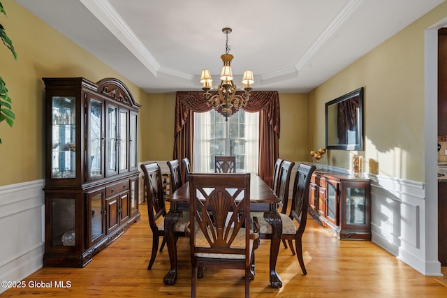 dining space with a raised ceiling, ornamental molding, an inviting chandelier, and light wood-type flooring