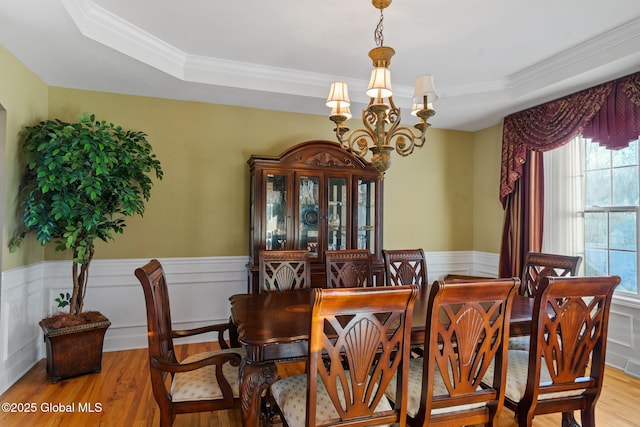 dining area with ornamental molding, a notable chandelier, light wood-type flooring, and a tray ceiling