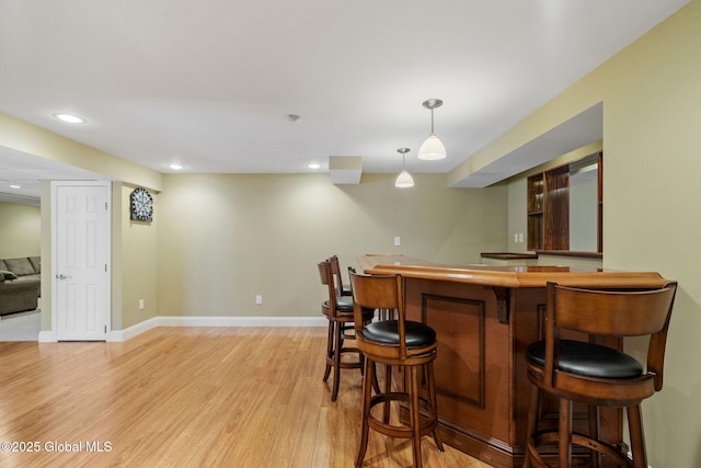 bar with hanging light fixtures and light hardwood / wood-style flooring