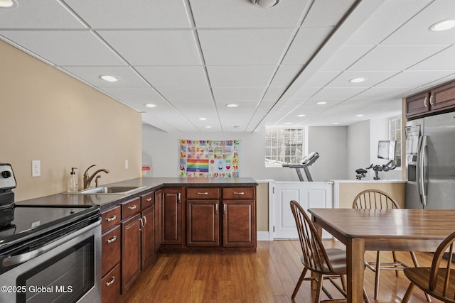 kitchen with a paneled ceiling, sink, kitchen peninsula, stainless steel appliances, and light wood-type flooring