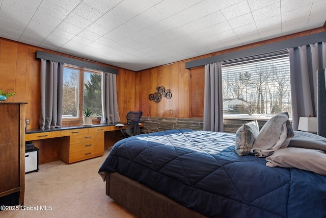 carpeted bedroom with wooden walls, built in desk, and multiple windows