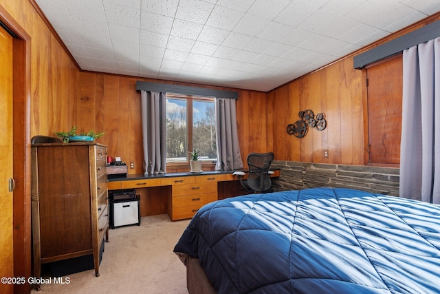 bedroom with built in desk, light colored carpet, and wooden walls