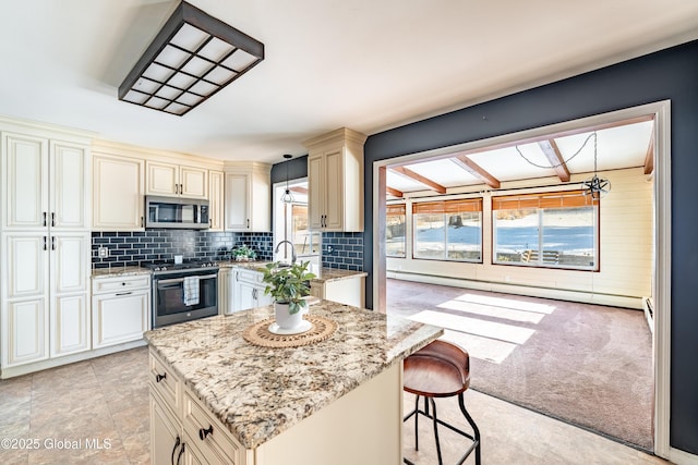 kitchen featuring pendant lighting, stainless steel appliances, light stone countertops, light colored carpet, and cream cabinetry