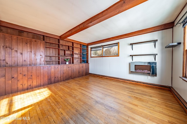 empty room with wooden walls, a fireplace, light hardwood / wood-style floors, built in shelves, and beamed ceiling