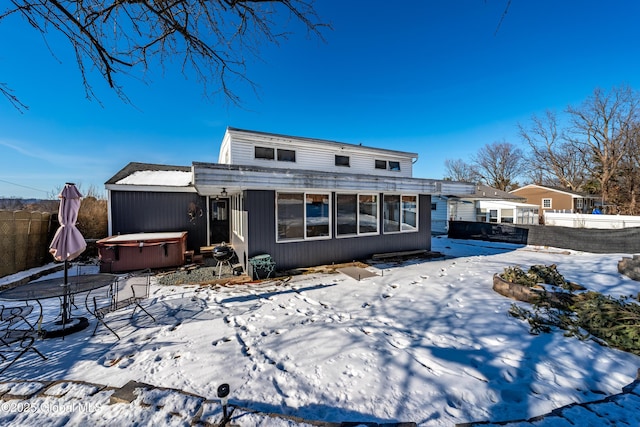 snow covered rear of property with a hot tub