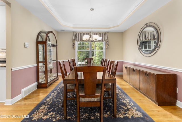 dining room with crown molding, a notable chandelier, a tray ceiling, and light wood-type flooring