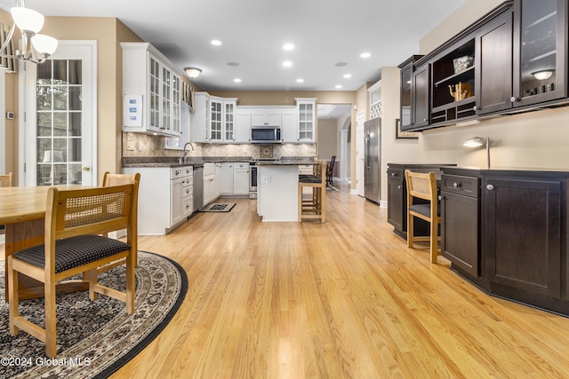 kitchen with appliances with stainless steel finishes, white cabinetry, a kitchen island, decorative backsplash, and light wood-type flooring