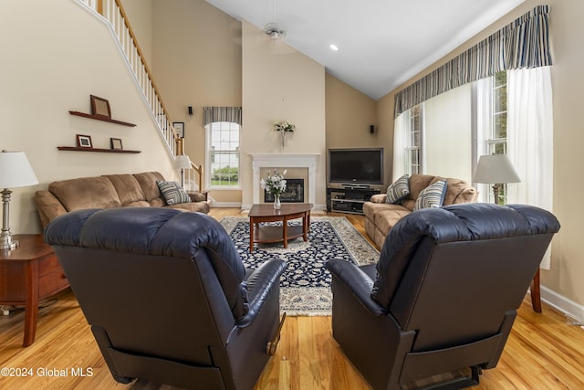 living room with ceiling fan, a high end fireplace, high vaulted ceiling, and light wood-type flooring