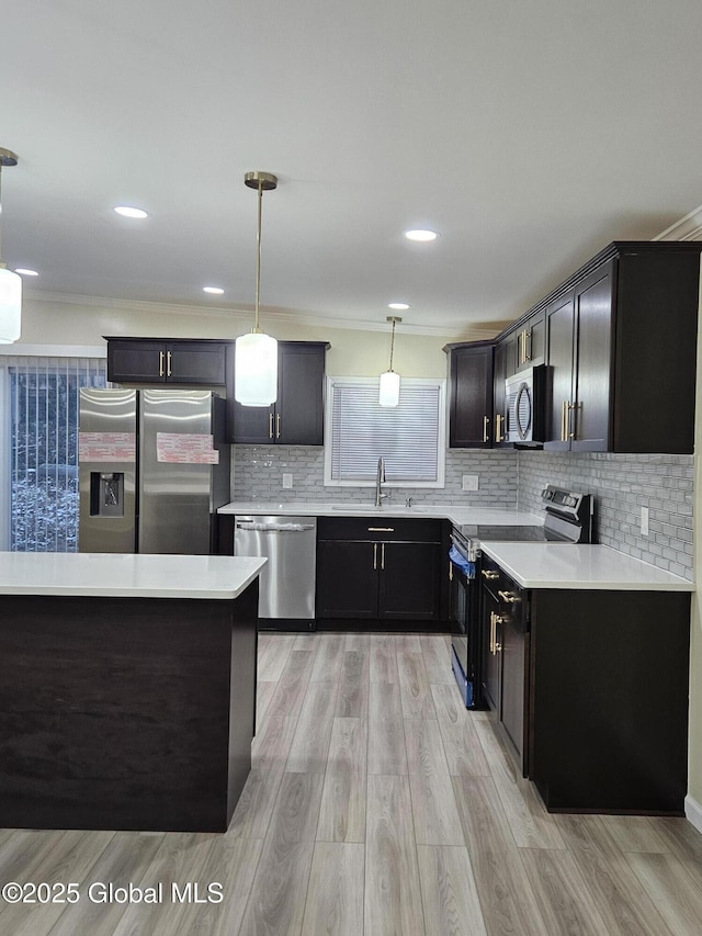 kitchen featuring sink, hanging light fixtures, light wood-type flooring, appliances with stainless steel finishes, and backsplash