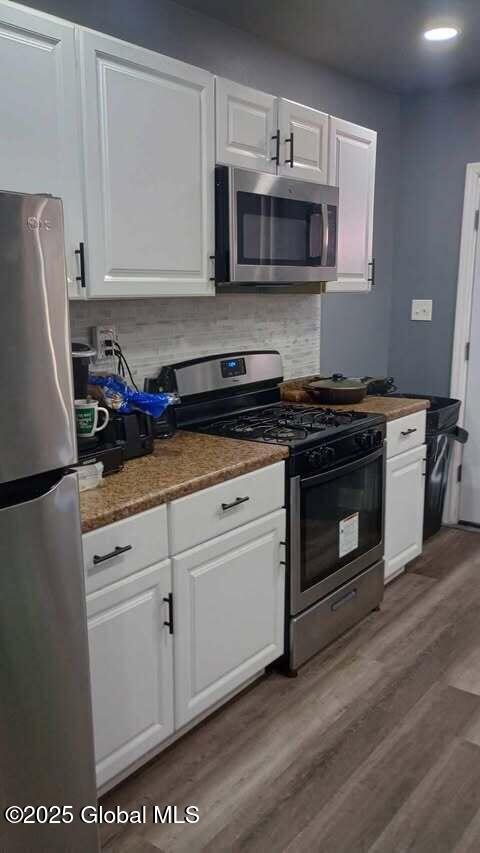 kitchen with wood-type flooring, appliances with stainless steel finishes, white cabinets, and decorative backsplash