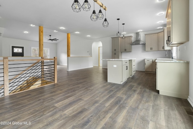 kitchen with hanging light fixtures, wall chimney exhaust hood, ceiling fan, a center island, and dark hardwood / wood-style flooring