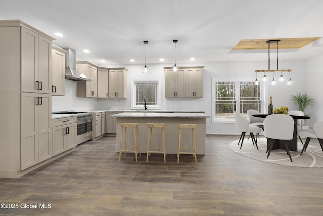 kitchen with wall chimney range hood, a kitchen bar, hanging light fixtures, and a center island